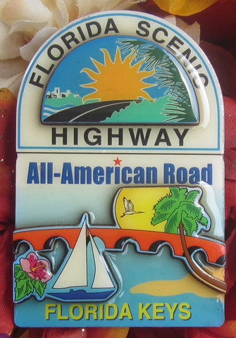 Magnet picture showing a 3D design symbolizing the part of US 1 in the "FLORIDA KEYS", calling it "FLORIDA SCENIC HIGHWAY", the "All-American Road", with a bridge, sailboat, palm tree, flower, bird and sunset.
