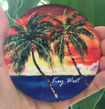 Hardboard Coaster picture showing a painting of palm trees in front of a sunset waterview.