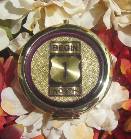 Compact Mirror picture showing a golden design of the US 1 sign "Begin" and "North".