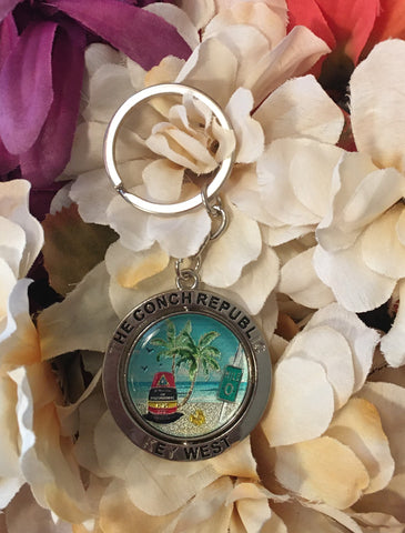 Key Chain composed of two parts: one center piece with a beach design showing the Southernmost Point, Mile 0, palm trees and conch shell; this part rotates horizontally. And the other part around the first piece, framing it and engraved with "The Conch Republic" and "Key West".