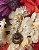 Key Chain showing a circular piece where "Key West" is engraved twice (top and bottom) and two shinny crystals are set; this circular piece is around a spinning piece in the shape and design of the Southernmost Point. This key chain also shows a hook (for example to attach the key chain onto a handbag).