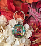 Front view of the key chain showing a beachside scenery with the Southernmost Point, Key West lighthouse, Mile 0 US 1 sign, palm trees, flowers, a rooster and "Key West".