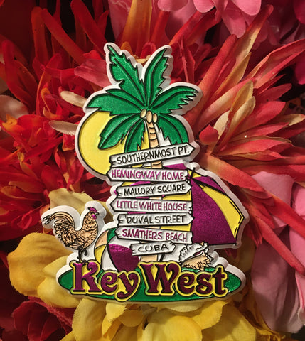 Magnet showing arrowed signs on a palm tree, directing to the Southernmost Point, Hemingway Home, Mallory Square, Little White House, Duval Street, Smathers Beach and to Cuba. With a rooster, a conch shell, an unbrella, a beach ball and "Key West".