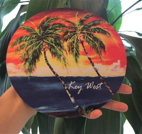 Mouse Pad round picture showing a painting of palm trees in front of a sunset waterview.