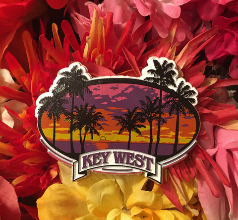 Magnet showing a beachside scenery with palm trees and a warm colored sunset. With "Key West".