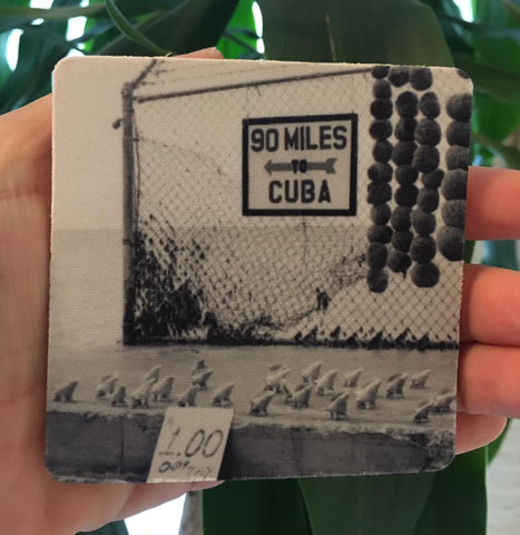Rubber Coaster showing a mid 20th century black and white picture of a "90 MILES TO CUBA" sign with an arrow pointing out to the sea and conch shells lined up on the cement, for sale at only $1 each! 