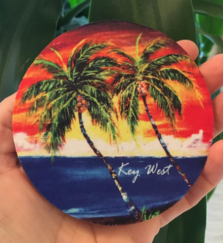 Rubber Coaster round picture showing a painting of palm trees in front of a sunset waterview.