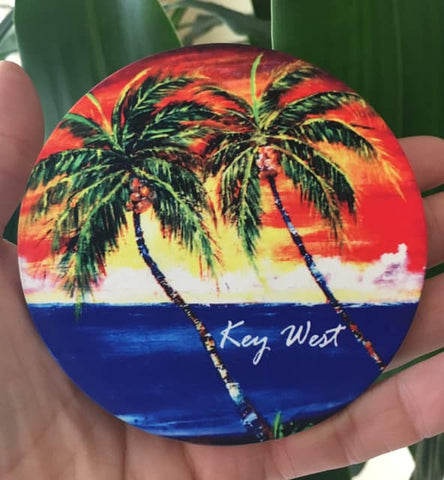 Sandstone Coaster round picture showing a painting of palm trees in front of a sunset waterview.