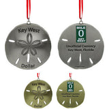 Metal ornament in the shape of a sandollar with "Key West Dollar" on the front. On the back: the Mile 0 sign and "Unofficial Currency", "Key West, Florida". The picture shows that item in silver and gold.