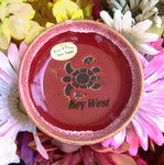 Red color glaze dish showing a sea turtle, a tiny fish and a seashell, with "Key West".